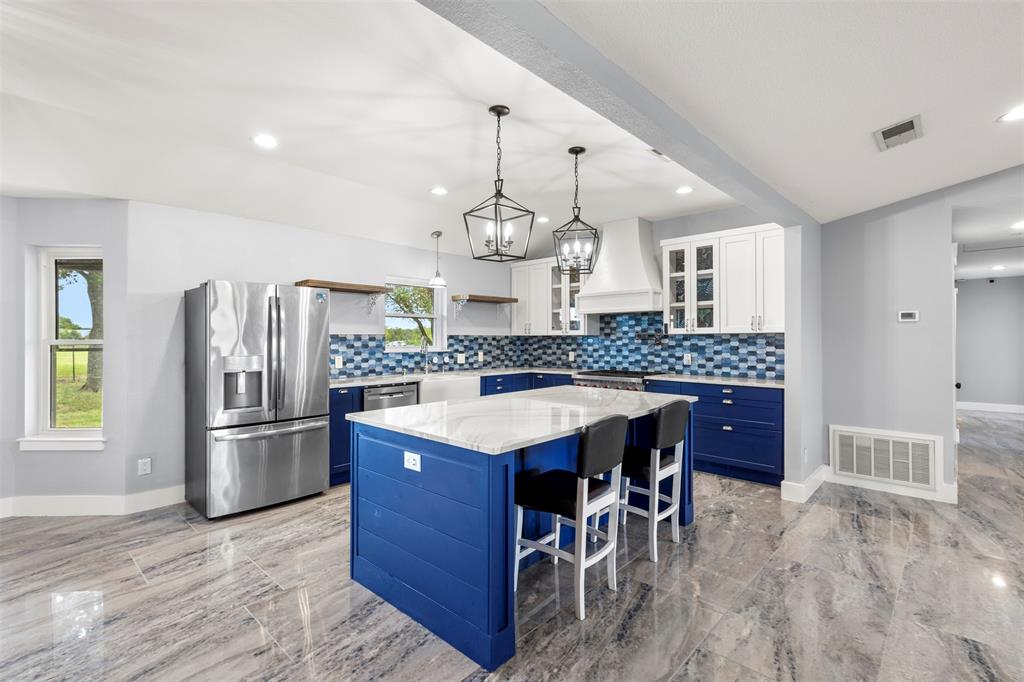 6754 Raymond Road Kaufman, TX 75142 - Photo 6 of 38 Spacious kitchen featuring a central island with countertop seating, stainless steel appliances, two-tone cabinetry, and a blue mosaic tile backsplash