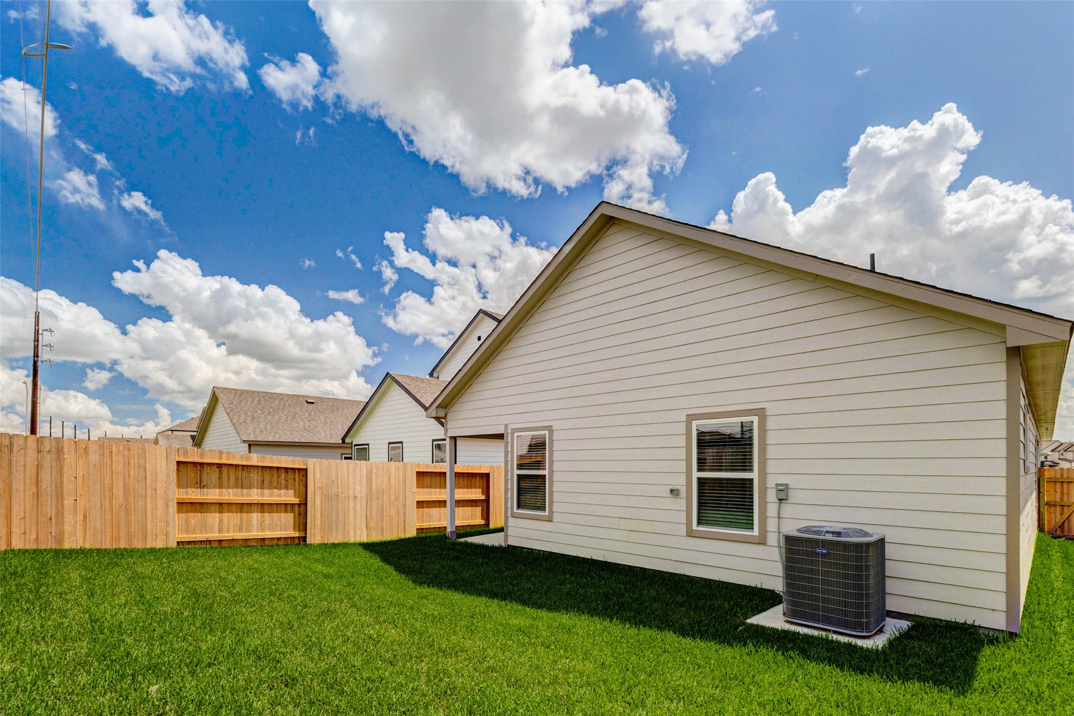 6467 Escondido Drive Rosharon, TX 77583 - Photo 29 of 32 Rear exterior view showcasing the fenced backyard, fresh green lawn, neutral siding, rear windows, and exterior HVAC unit. The private yard offers manageable outdoor space for relaxing, pets, play, or simple weekend enjoyment, with clean new-construction finishes and plenty of sunshine.