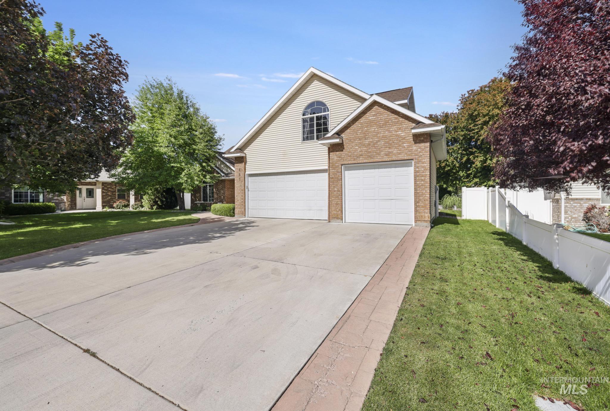 467 Wildrose Loop Twin Falls, ID 83301 - Photo 2 of 46 Brick and siding exterior featuring an arched window, a two-car garage, a concrete driveway with a brick border, mature trees, and a white privacy fence