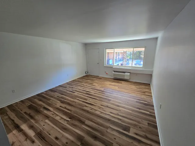 a view of an empty room with wooden floor and a window