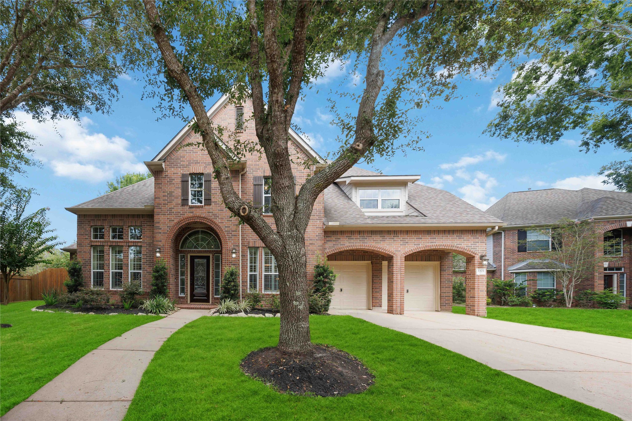 3303 Raleigh Row Missouri City, TX 77459 - Photo 2 of 50 Elegant brick home with charming arched windows, a welcoming front porch area, and a spacious two-car garage, surrounded by lush landscaping and mature trees.
