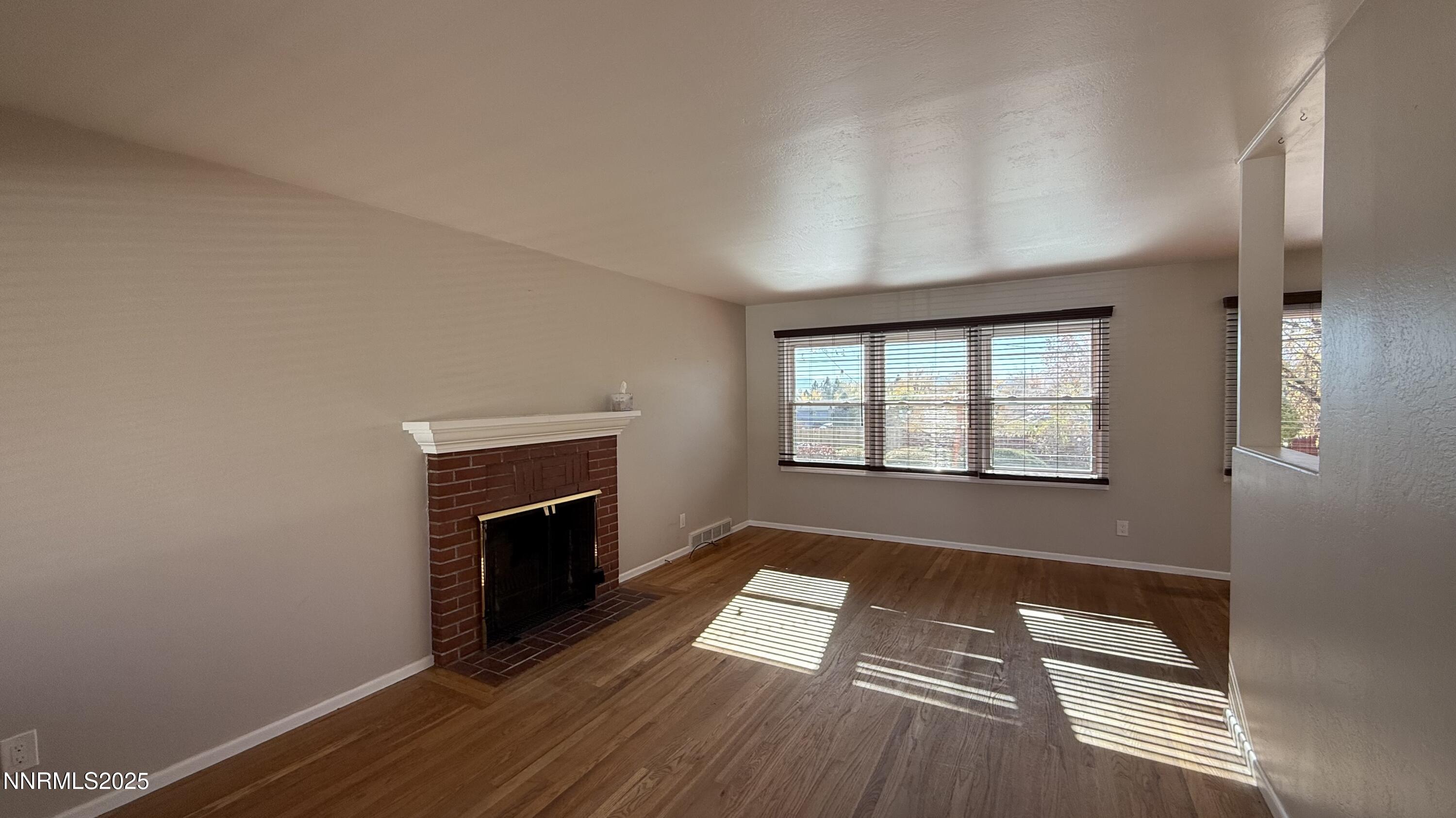 1455 Wesley Drive Reno, NV 89503 - Photo 3 of 27 an empty room with wooden floor fireplace and windows