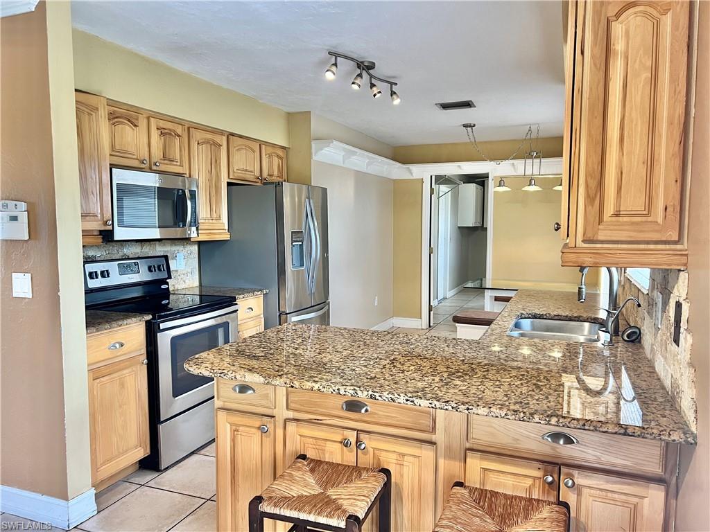 18581 Tampa Road Fort Myers, FL 33967 - Photo 1 of 25 Kitchen featuring appliances with stainless steel finishes, tasteful backsplash, light stone counters, sink, and light tile patterned flooring
