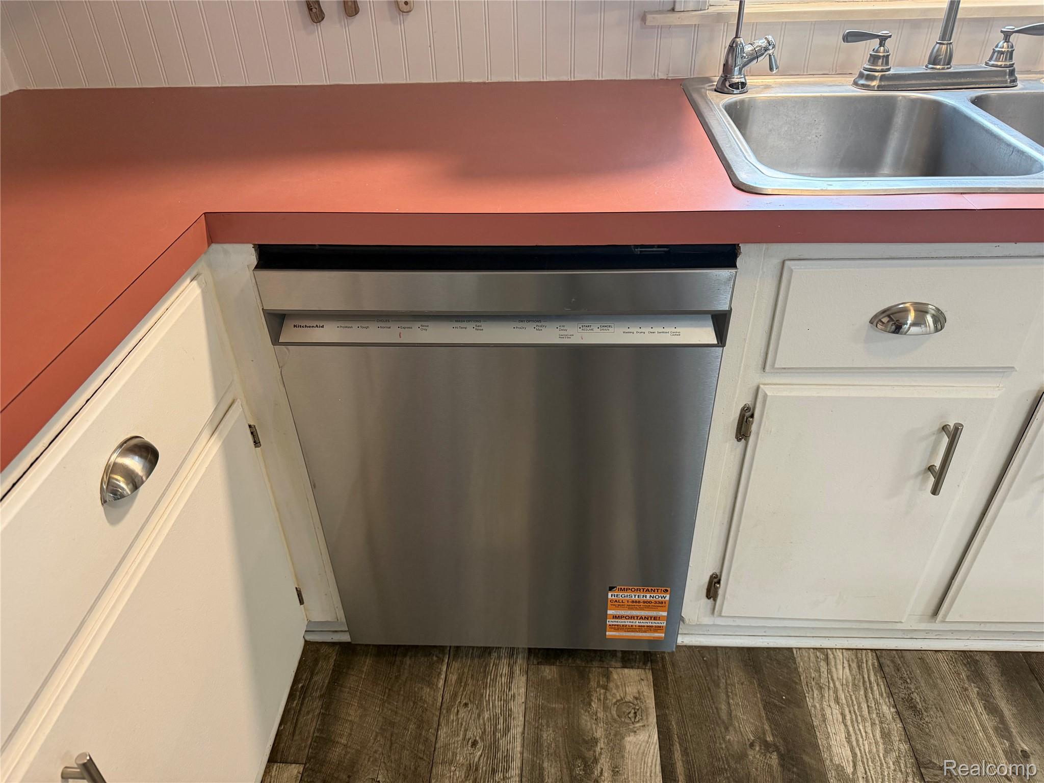 2402 Mertz Road Caro, MI 48723 - Photo 11 of 26 Updated kitchen featuring stainless steel dishwasher, white cabinetry with brushed nickel hardware, coral laminate countertops, and wood-finish flooring throughout the cooking and prep area