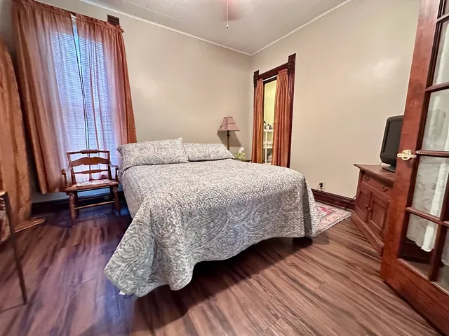 a bedroom with a bed wooden floor and a flat tv screen on a dresser
