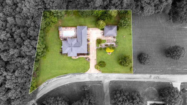 an aerial view of a residential houses with outdoor space and trees all around