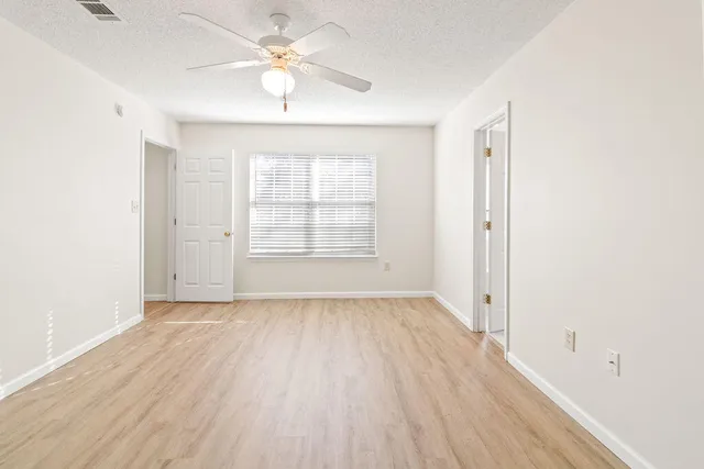 an empty room with wooden floor chandelier fan and windows
