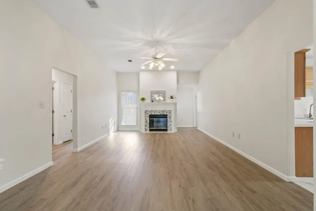 an empty room with wooden floor fireplace and chandelier fan