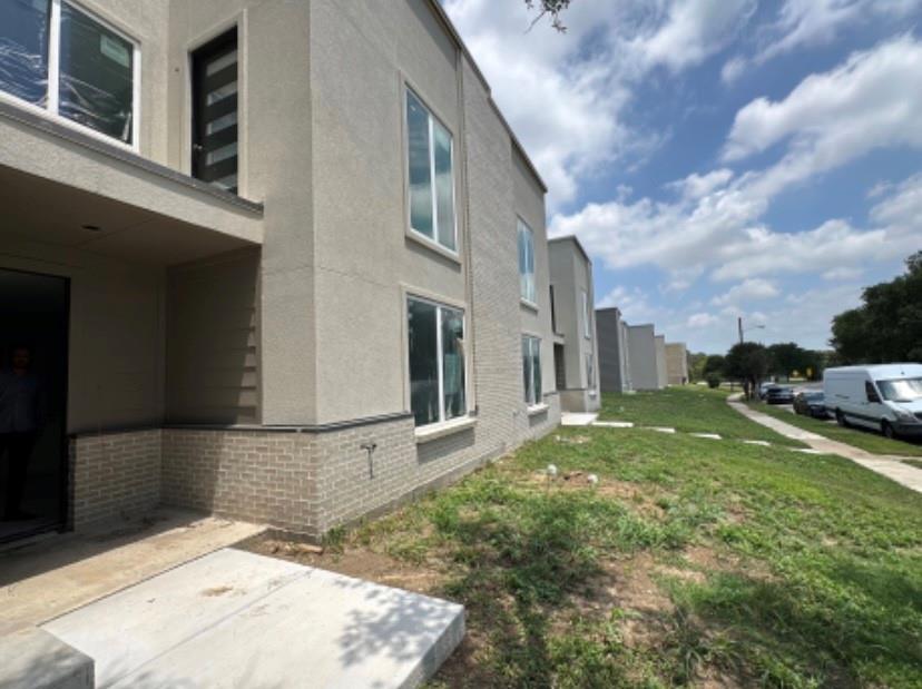 View of side of property featuring brick siding, stucco siding, a patio area, a lawn, and a residential view