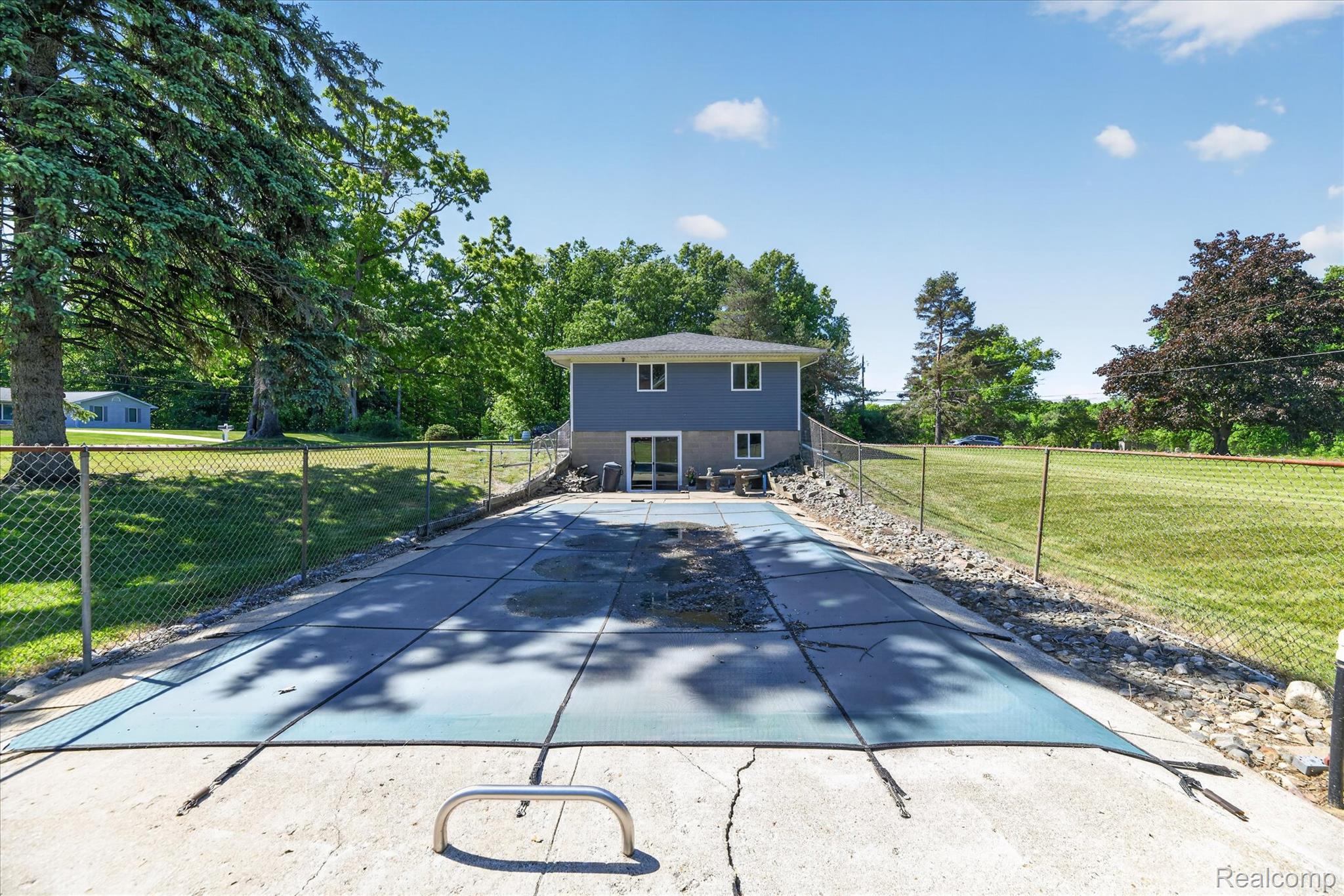 2250 Montague Road Davison, MI 48423 - Photo 43 of 45 Expansive backyard featuring a covered inground pool, concrete patio, chain-link fencing, mature trees, and a two-story residence with blue siding
