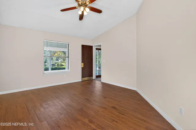 an empty room with wooden floor chandelier fan and windows