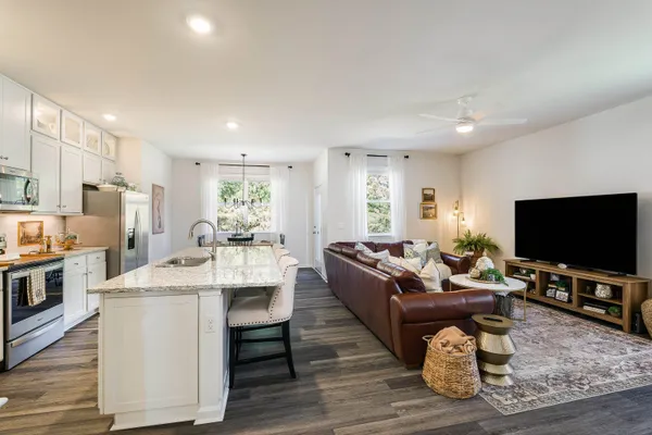 a kitchen with stainless steel appliances granite countertop a stove top oven a refrigerator a sink and white cabinets with wooden floor