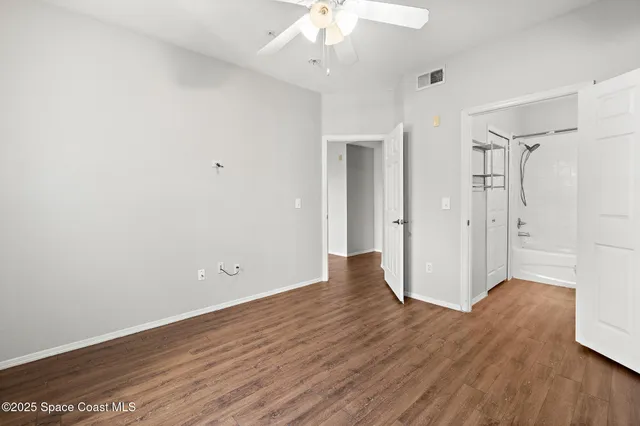 an empty room with wooden floor chandelier fan and windows