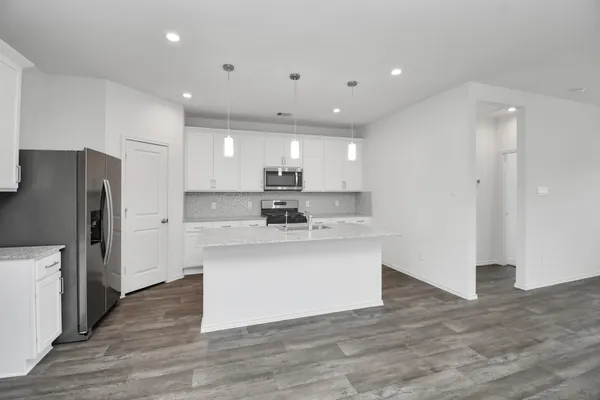 a kitchen with stainless steel appliances granite countertop a refrigerator a sink a stove a microwave and white cabinets with wooden floor