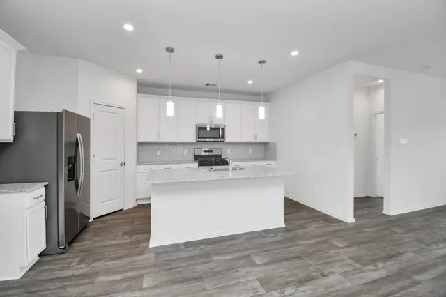 a kitchen with stainless steel appliances granite countertop a refrigerator a sink a stove a microwave and white cabinets with wooden floor