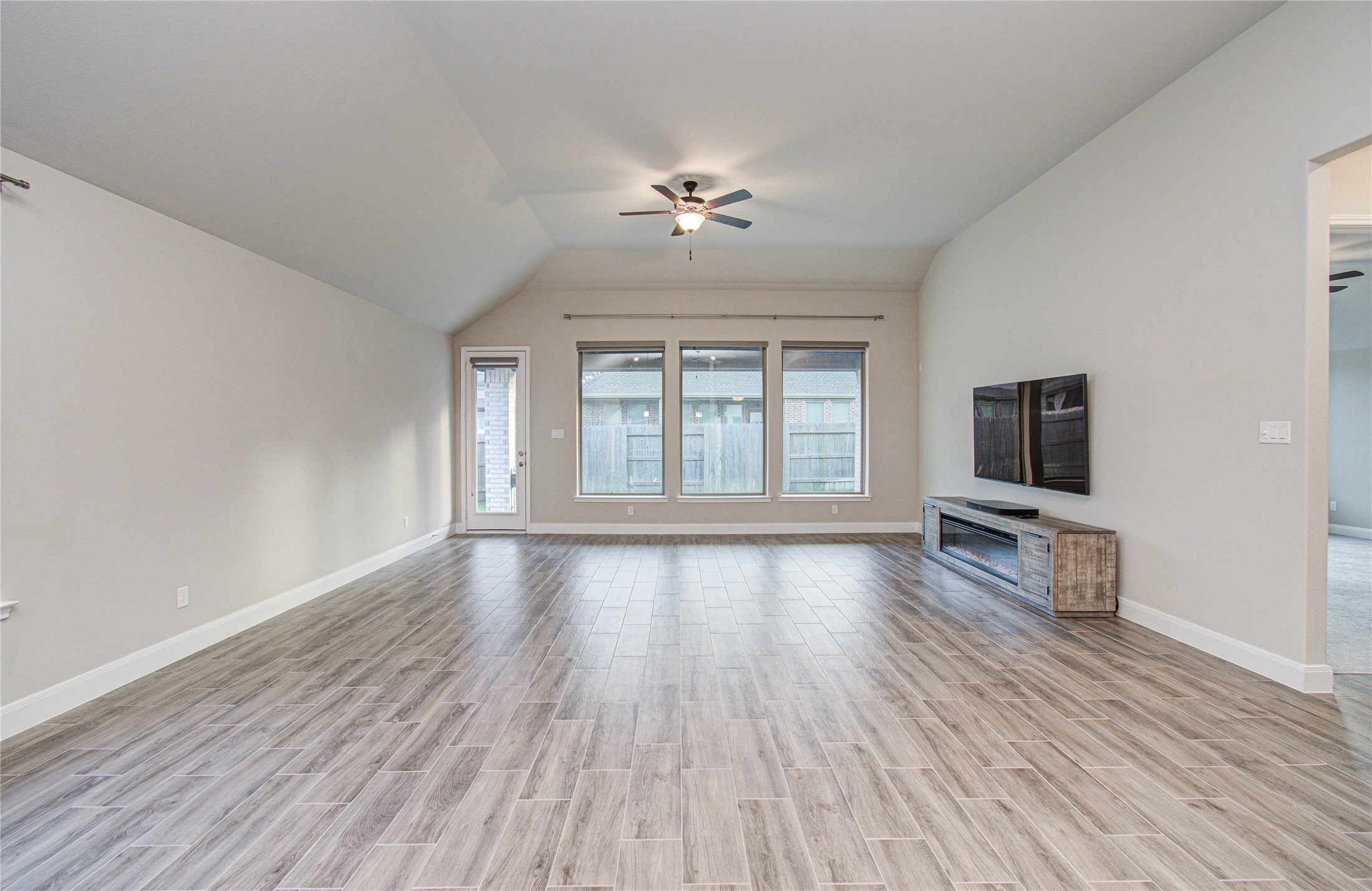 17344 Grand Canyon Road Conroe, TX 77302 - Photo 33 of 49 Spacious living room with wood-look tile flooring, neutral walls, and a ceiling fan. It features large windows for natural light, a wall-mounted TV, and a modern entertainment unit. Ideal for comfortable living and entertainment.