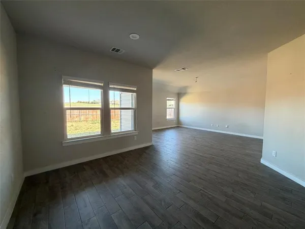 a view of an empty room with wooden floor and window