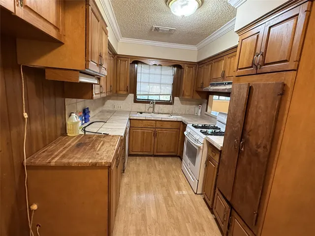 a kitchen with stainless steel appliances granite countertop a refrigerator a sink dishwasher a stove and white countertops with wooden floor