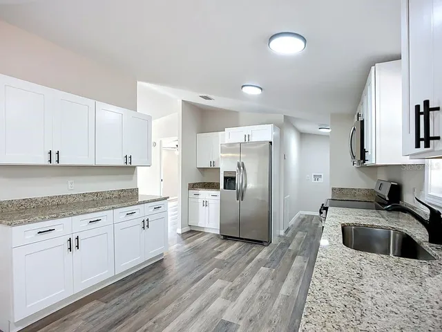 a kitchen with granite countertop a refrigerator a sink a stove a microwave and cabinets