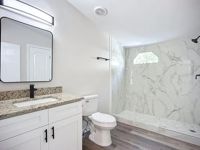 a bathroom with a granite countertop sink toilet a mirror and shower
