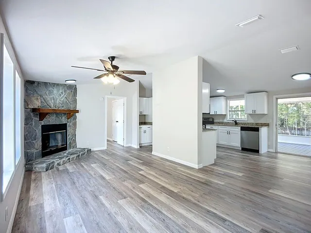a view of a livingroom with a fireplace a ceiling fan and wooden floor