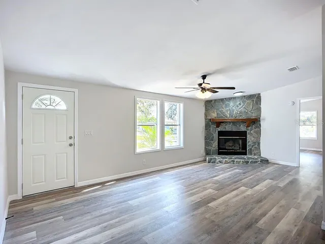 an empty room with windows fireplace and a ceiling fan
