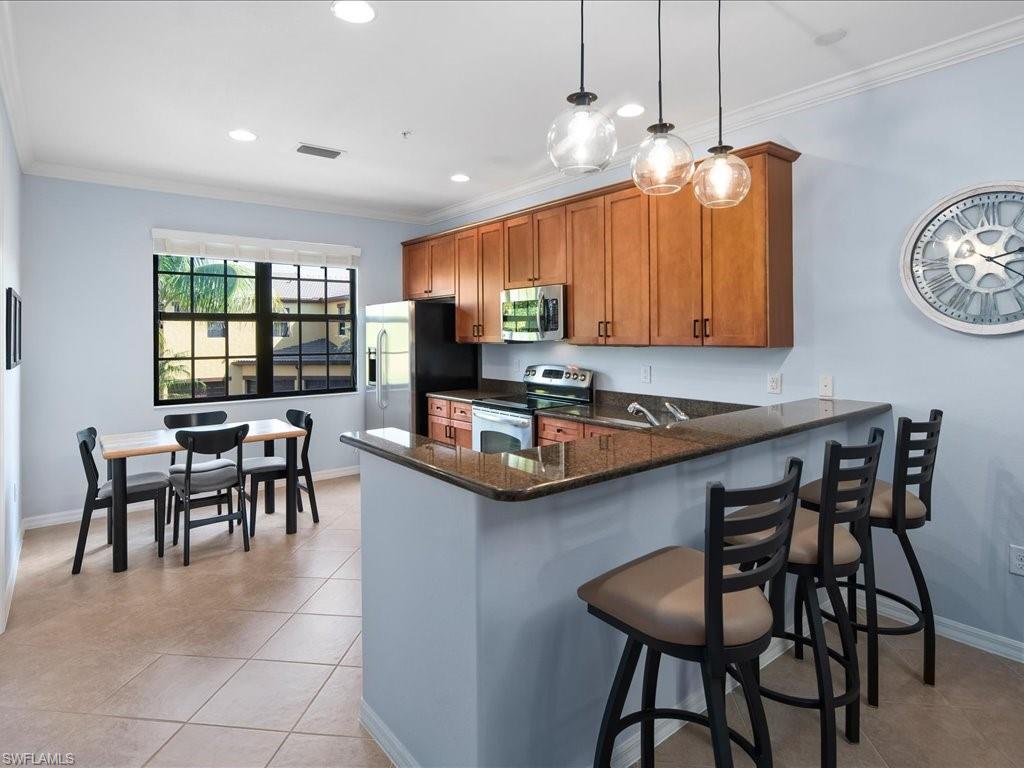 8985 Cambria Circle, Unit 215 Naples, FL 34113 - Photo 12 of 36 a kitchen with kitchen island granite countertop a table chairs sink and cabinets