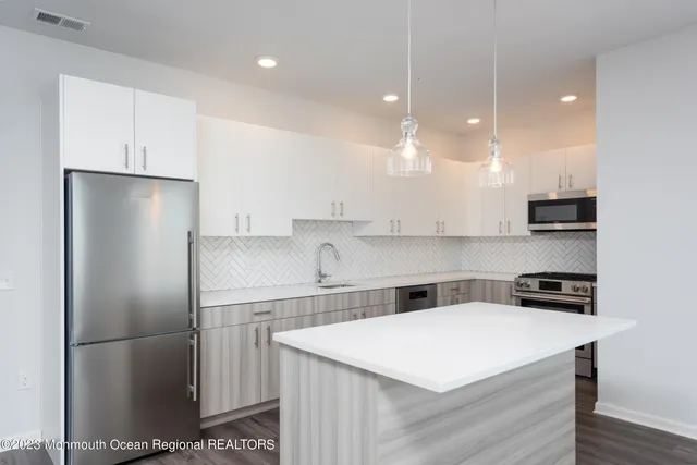 a kitchen that has a refrigerator a stove a sink and white cabinets with wooden floor