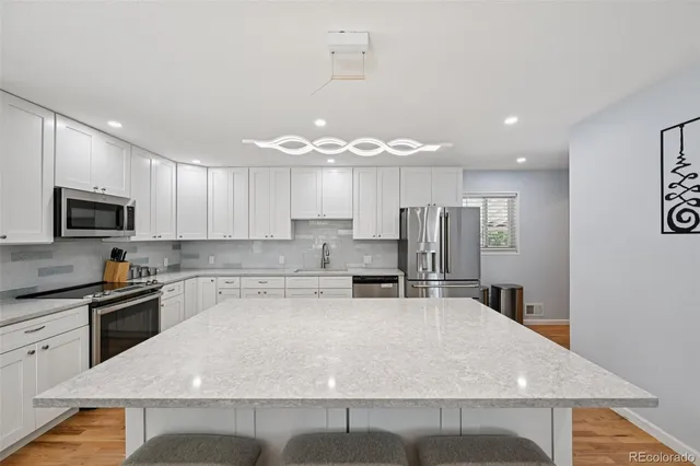 a kitchen with stainless steel appliances granite countertop a stove top oven a sink a refrigerator and white cabinets