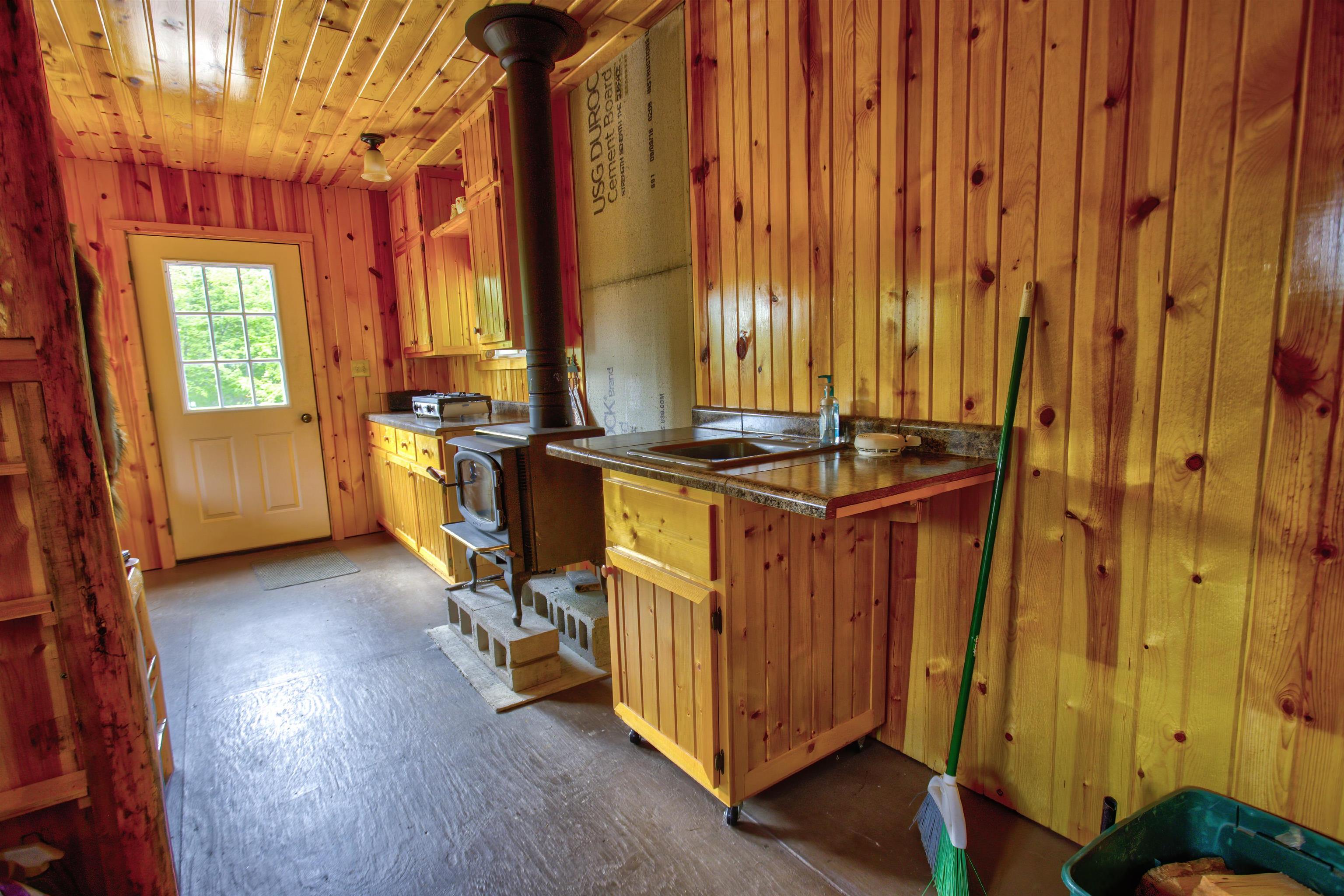 4194 Nels Lake Road Ely, MN 55731 - Photo 12 of 27 Kitchen featuring a wood stove, stainless steel counters, wooden walls, open shelves, and wooden ceiling
