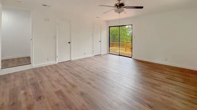 an empty room with wooden floor fan and windows