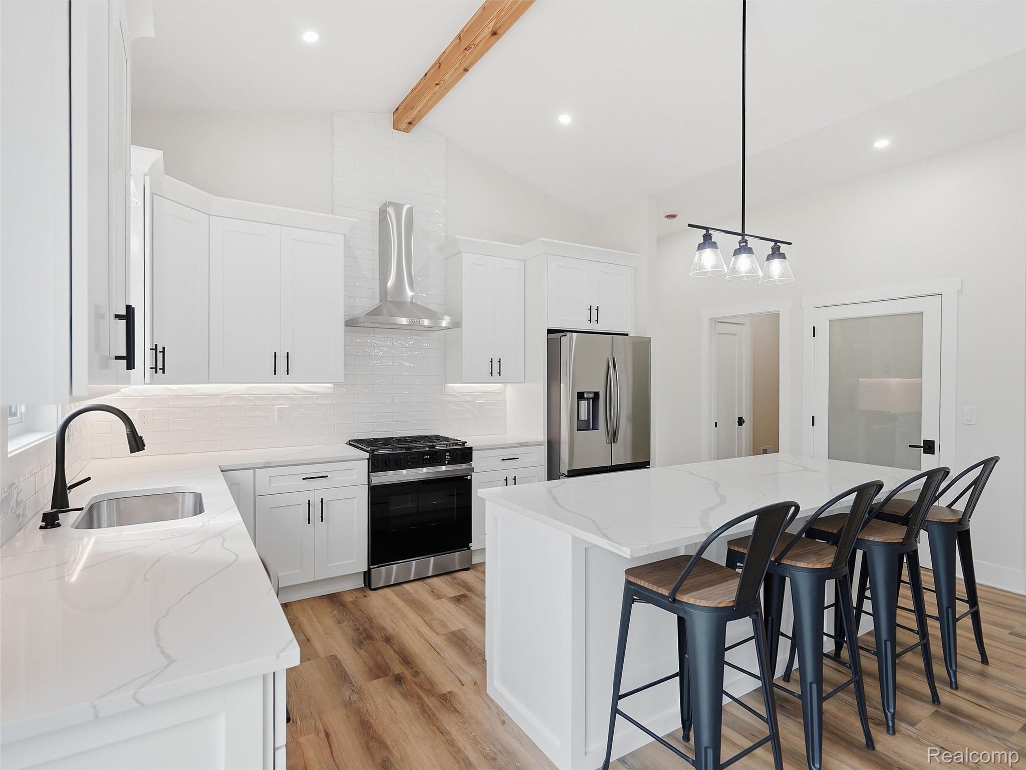 77850 Angling Road Richmond, MI 48062 - Photo 18 of 54 Modern kitchen featuring white cabinetry, stainless steel appliances, wood-finish flooring, a central island with countertop seating, and a vaulted ceiling with an exposed beam