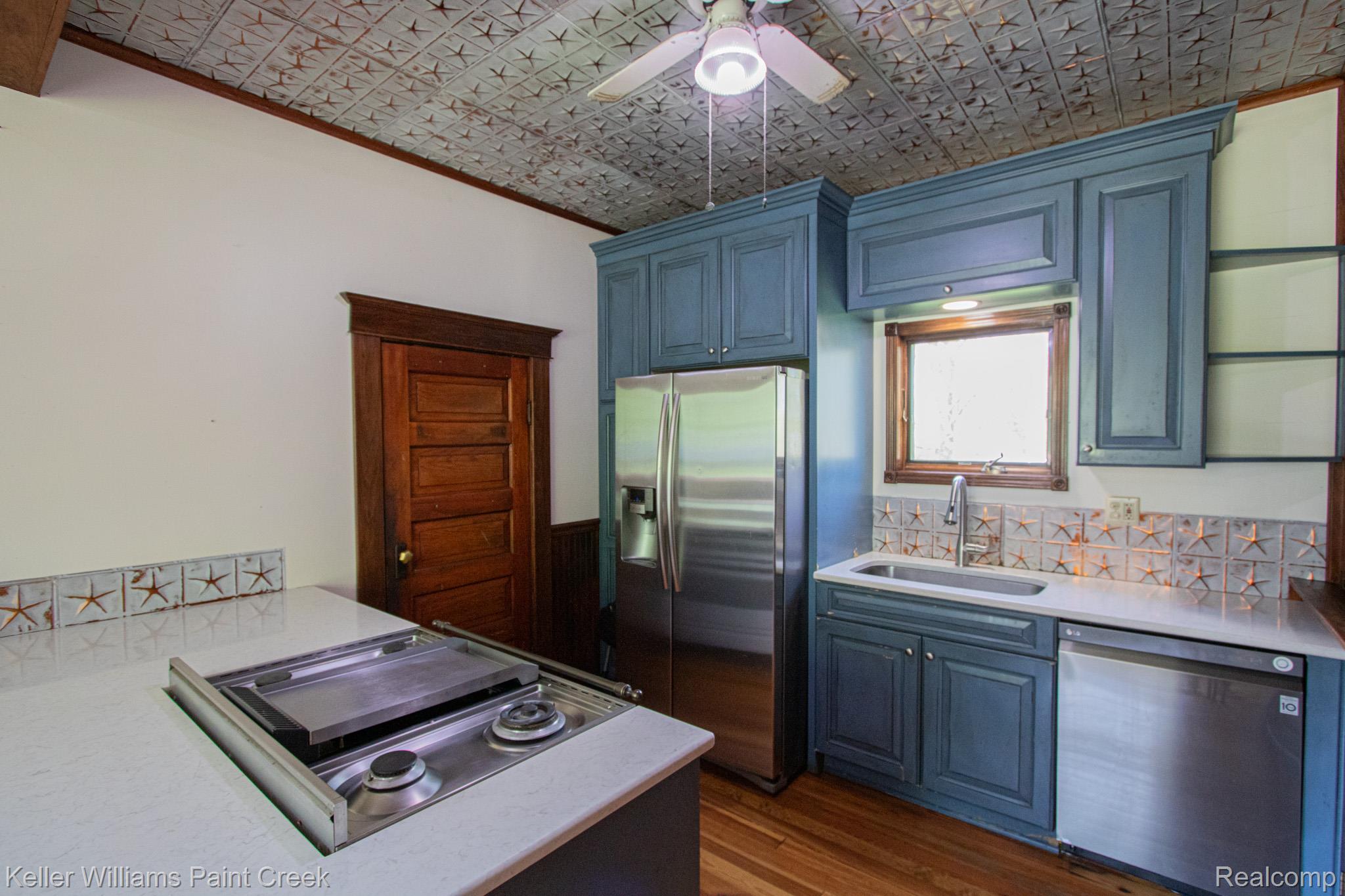 Kitchen with stainless steel appliances, a ceiling fan, ornamental molding, dark wood finished floors, and an ornate ceiling