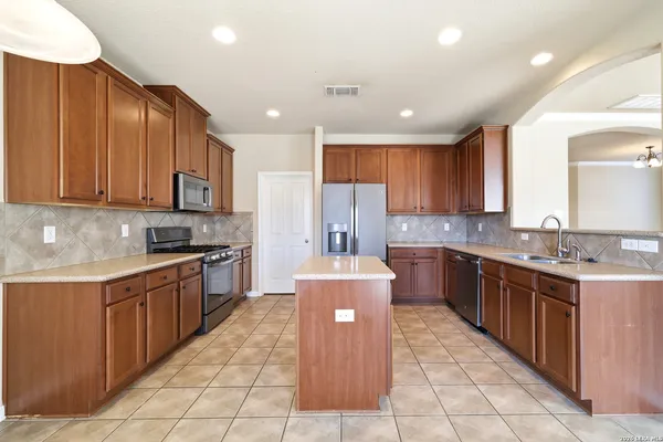 a large kitchen with stainless steel appliances wooden cabinets and a stove top oven