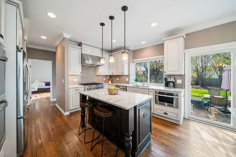 a kitchen with kitchen island a stove a refrigerator a sink dishwasher with a dining table and chairs with wooden floor