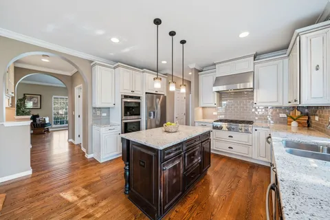 a kitchen with stainless steel appliances granite countertop a stove top oven a sink dishwasher and a refrigerator with wooden floor
