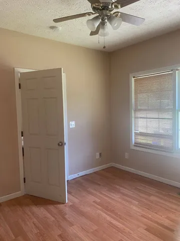 an empty room with wooden floor chandelier fan and windows