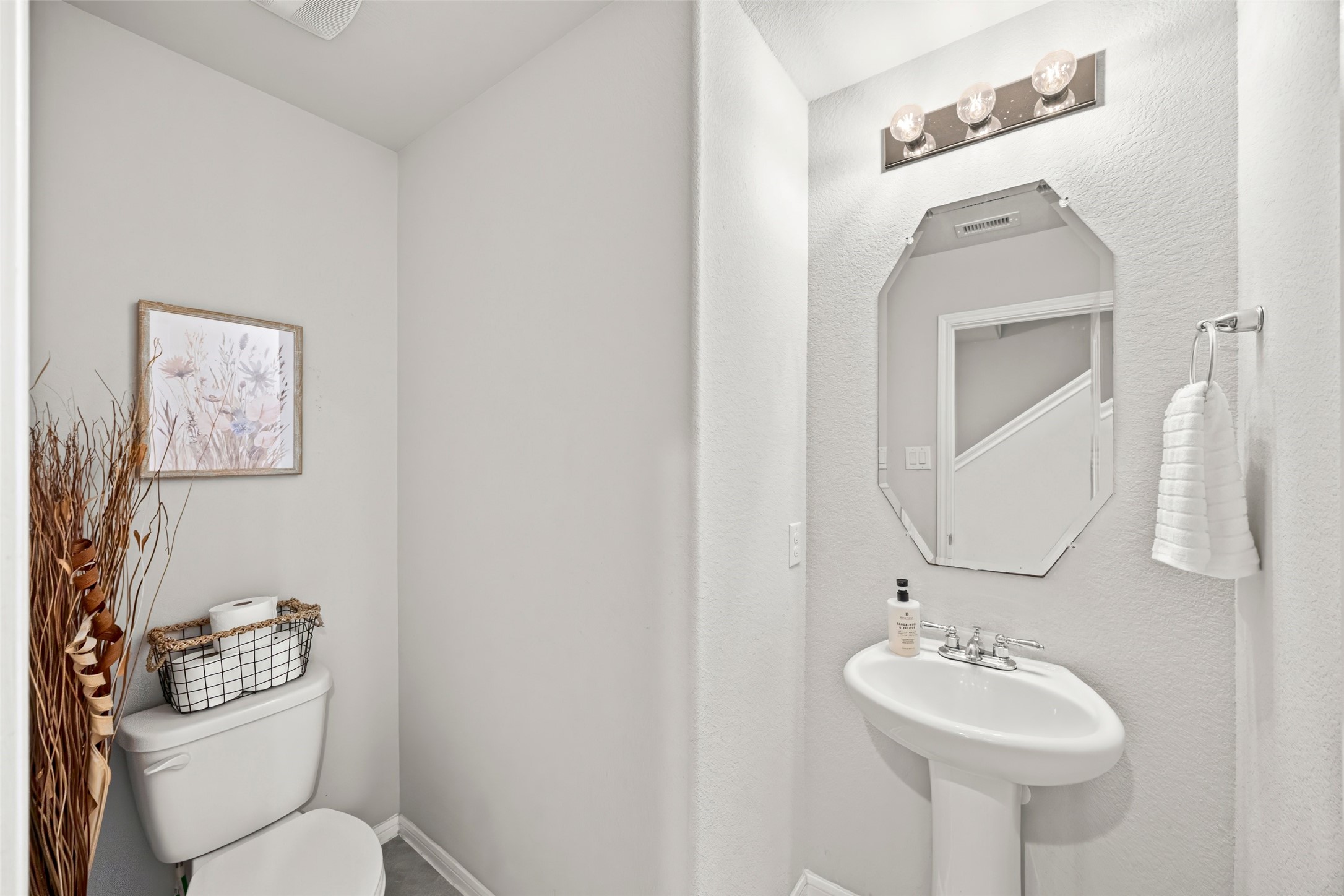 8026 Farthing Lane Rosharon, TX 77583 - Photo 10 of 13 This is a small, modern half-bathroom with a pedestal sink and stylish mirror. It features a neutral color palette, wall-mounted lighting, and simple decor, including a framed artwork and decorative basket.
