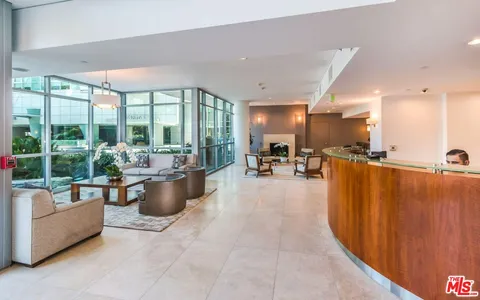 a living room with furniture potted plant kitchen view and large windows