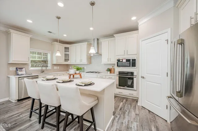 a kitchen with stainless steel appliances granite countertop a refrigerator a stove a sink a dining table and chairs with wooden floor