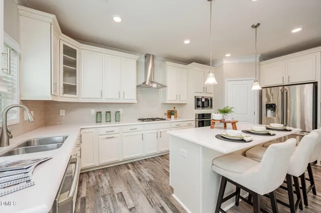 a kitchen with stainless steel appliances granite countertop a sink a stove a refrigerator and white cabinets with wooden floor