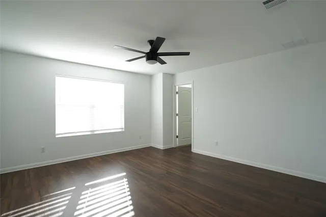 an empty room with wooden floor window and ceiling fan