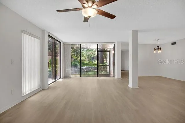 a view of an empty room with chandelier fan and windows