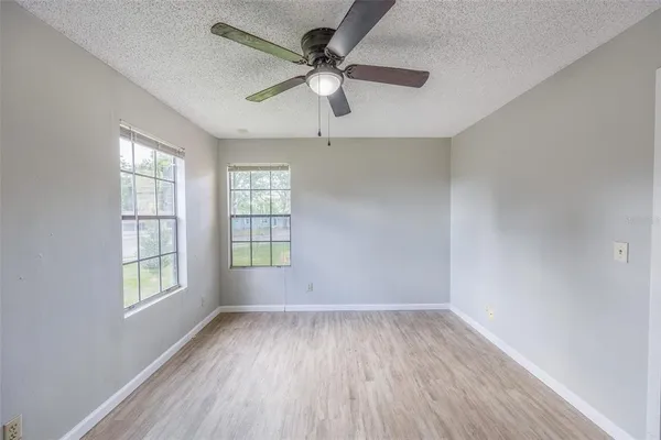 an empty room with wooden floor ceiling fan and windows