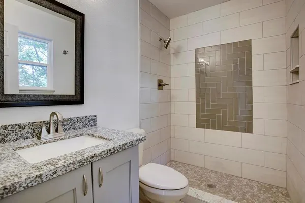 a bathroom with a granite countertop sink a toilet a mirror and shower