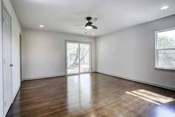 an empty room with wooden floor chandelier fan and windows