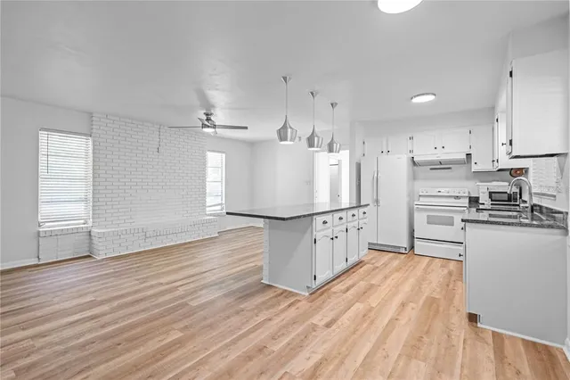 a kitchen with stainless steel appliances granite countertop a refrigerator a sink dishwasher a stove and white countertops with wooden floor