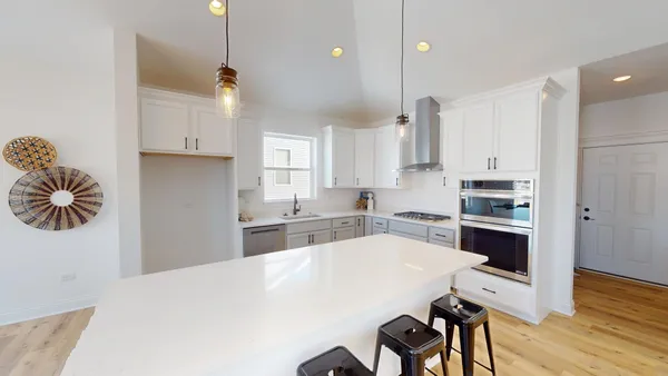 a kitchen with stainless steel appliances kitchen island granite countertop a stove a sink a refrigerator and white cabinets with wooden floor