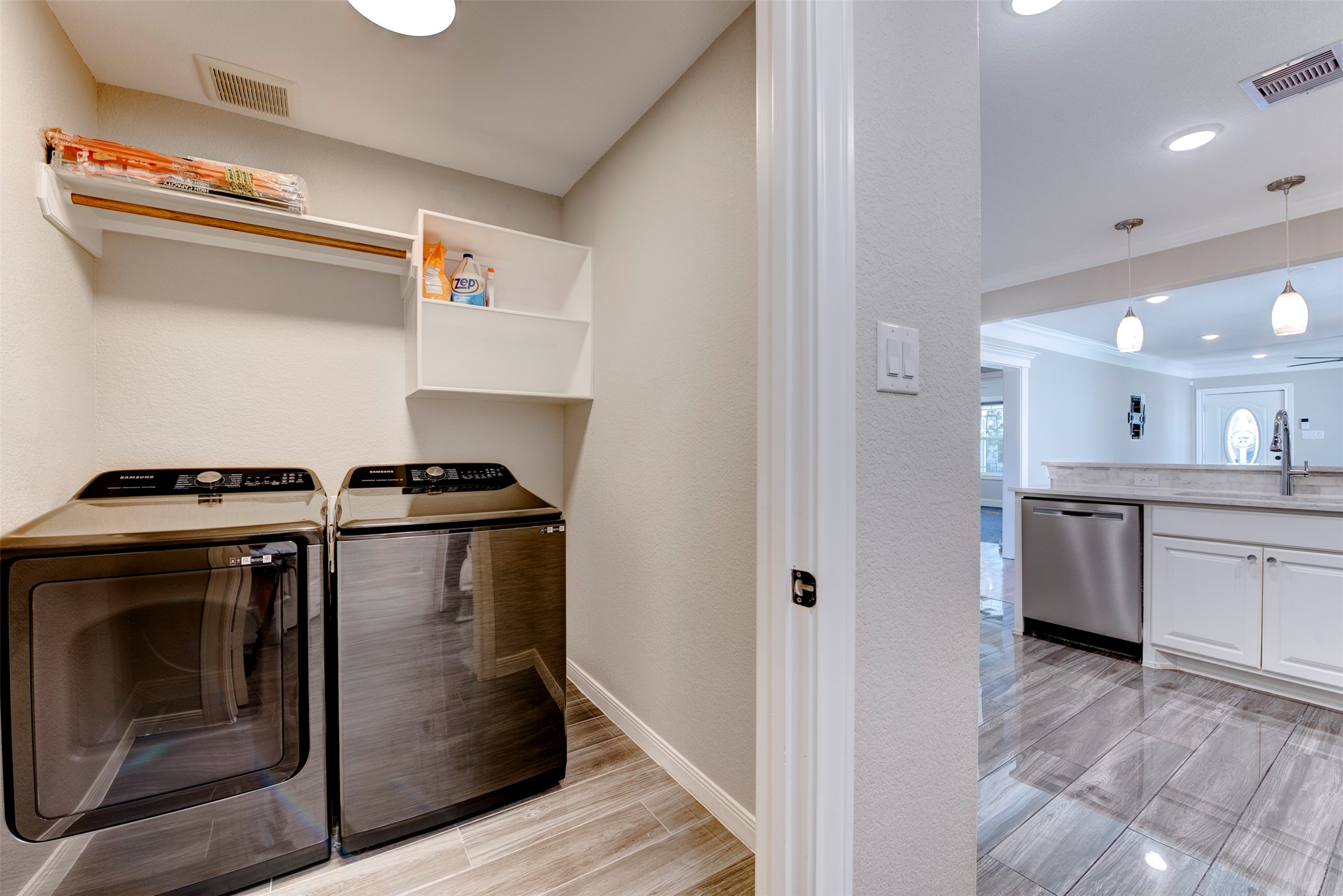 109 Dresden Street Houston, TX 77012 - Photo 22 of 43 This photo showcases a modern laundry area with a sleek washer and dryer, adjacent to an open-plan kitchen featuring stainless steel appliances, pendant lighting, and polished tile flooring.