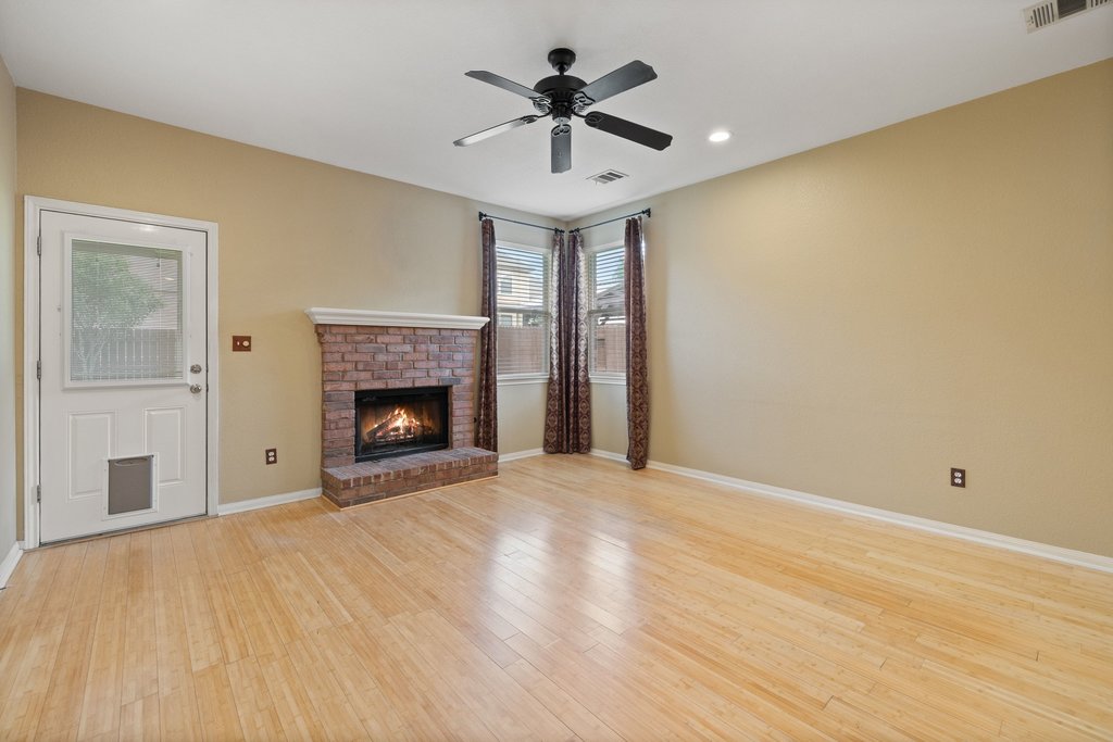 347 Spring Drive Kyle, TX 78640 - Photo 22 of 40 A well-lit living area features a brick fireplace and warm wood flooring.